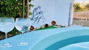 Ein Schwimmbecken mit zwei klaren Gläsern am Rand, einer Wandmalerei eines Pferdes und einer Steinmauer im Hintergrund.