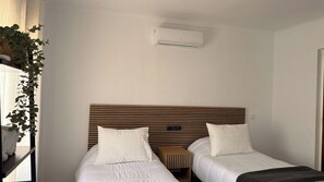 Camera d'albergo con due letti, una testiera in legno, un comodino e un condizionatore d'aria a parete.