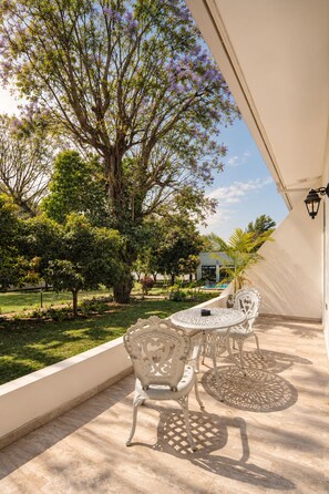 Un patio al aire libre con mesa y sillas, rodeado de follaje y un árbol.