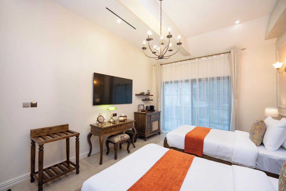 A hotel room with two beds, a desk with a chair, a television, and a window with curtains.