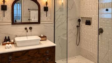 Un baño moderno con ducha envuelta en vidrio, suelo de mármol, tocador de madera con un espejo grande y luces empotradas.