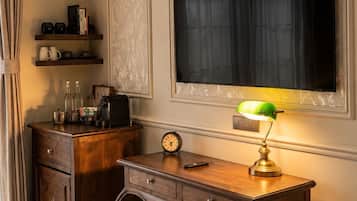Una habitación con escritorio, una silla, una estantería con libros y objetos decorativos, un reloj y un televisor montado en la pared.