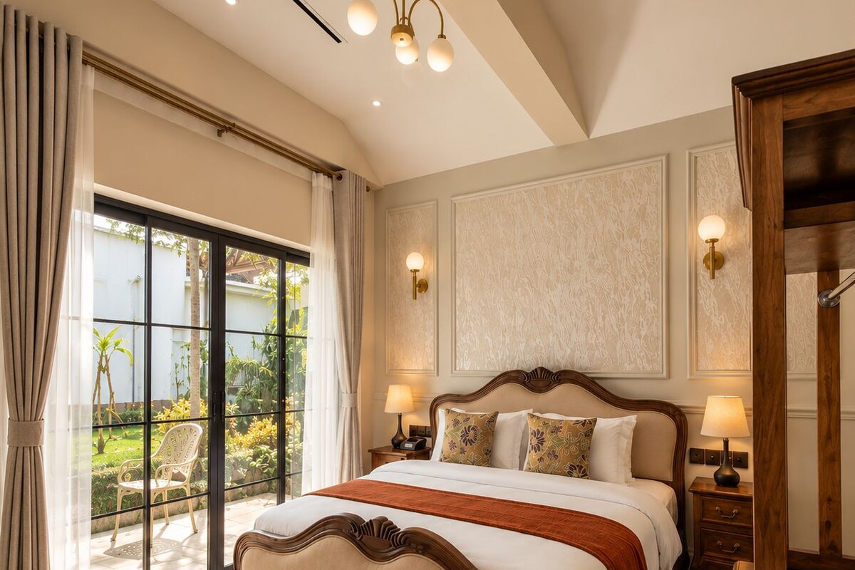 A spacious bedroom with a large bed, a wooden headboard, two bedside lamps, and a view of a garden through a sliding glass door.