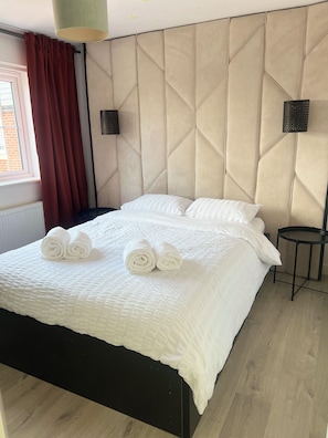 A hotel room with a large bed, a headboard with a geometric pattern, a small round table, and a window with curtains.