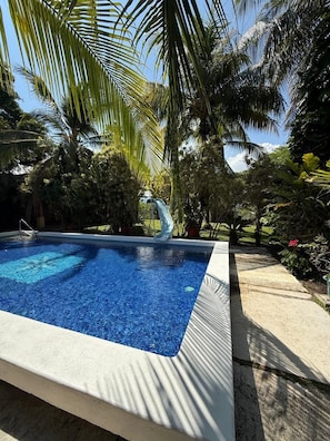 Uma piscina com superfície de água azul translúcida, cercada por vegetação exuberante e palmeiras.