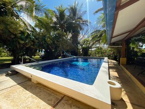 A rectangular swimming pool with a white edge, surrounded by lush greenery and palm trees. - 3BR Villa  Private Pool by Carara Park (lagunillas)