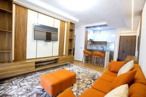 Ein modernes Wohnzimmer mit einer Couch, einem Hocker und einer Küchenzeile mit Barhocker.