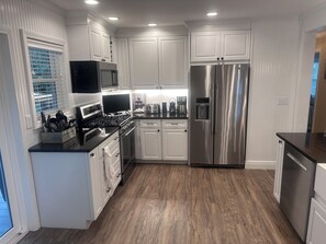 A modern kitchen with white cabinetry, stainless steel appliances, and a wooden floor.