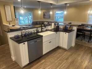 A kitchen with a central island, white cabinetry, and a black countertop. There are pendant lights, a window with blinds, and a dining area visible. - Summer and Winter Escape 20 Seconds From the Lake With Lake Views (Findley Lake)