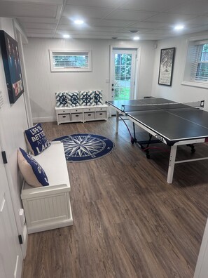 Una habitación con mesa de ping pong, un banco blanco con cojines de temática náutica y una alfombra con forma de brújula.