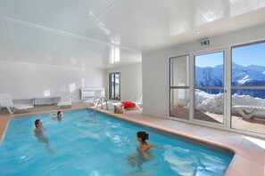 Ein Hallenbad mit freiem Blick auf schneebedeckte Berge durch große Fenster.