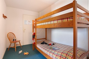 Ein Schlafzimmer mit Etagenbetten, einem Holzrahmen, einer Karo-Bettdecke, einem Stuhl mit einem Stofftier und einer Tür mit einem Hinweis.