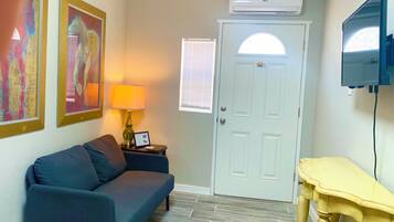 A room with a sofa, a lamp, a door, and a television mounted on the wall.