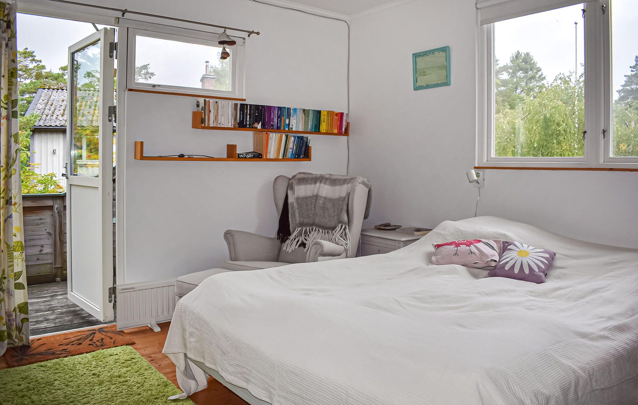 A bedroom with a bed, a chair, a bookshelf, and a window.