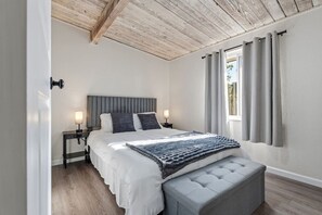 Une chambre à coucher avec un lit, des lampes de chevet, un banc et une fenêtre avec des rideaux.