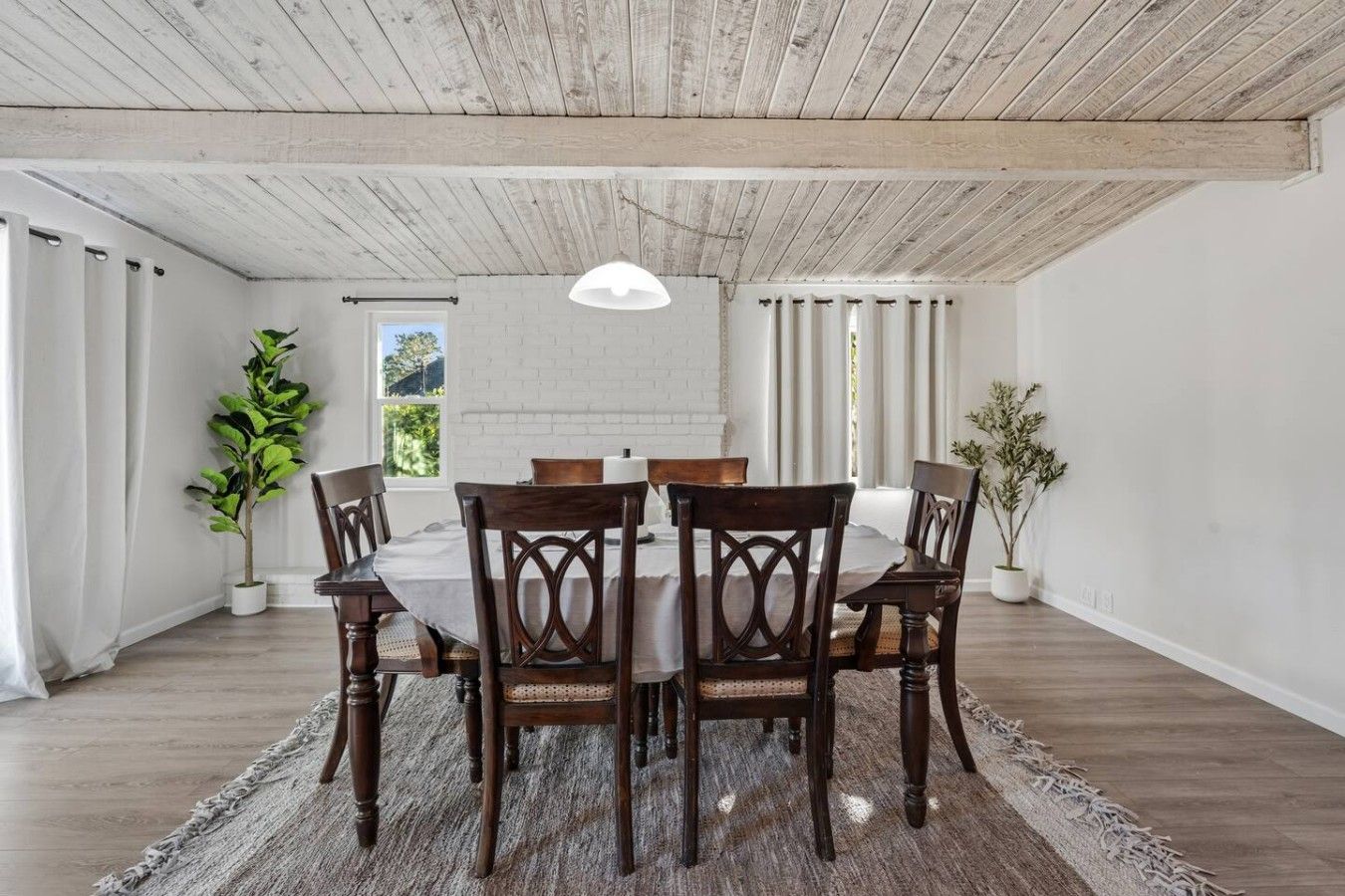 A dining area with a wooden table and chairs, a hanging light fixture, and a view of the outdoors.