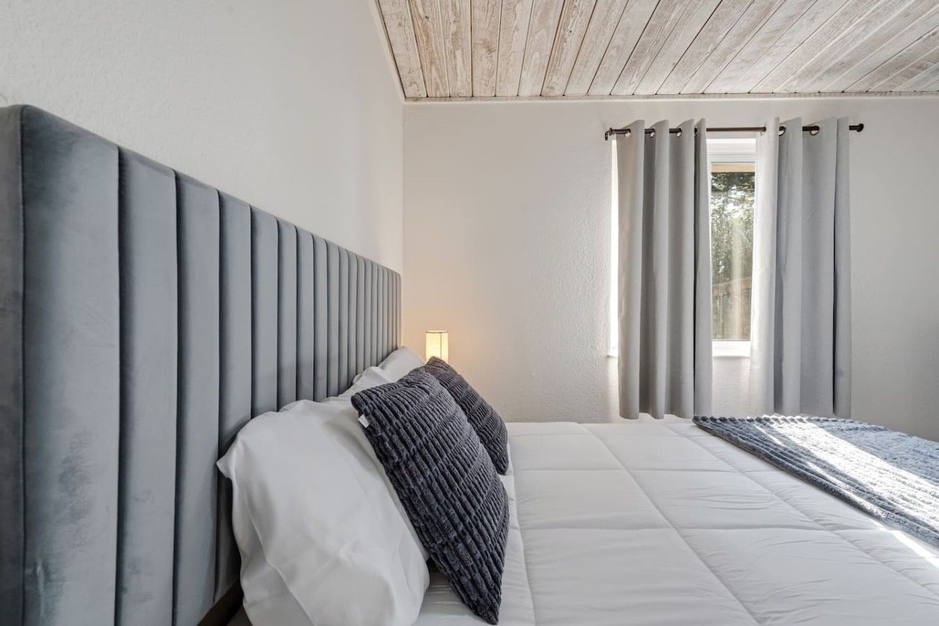 Un dormitorio con una cama grande, cabecera y ventana con cortinas.