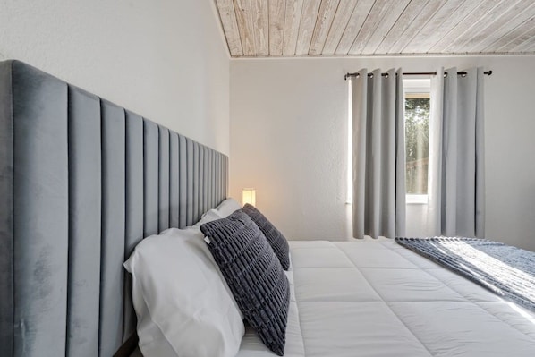 Un dormitorio con una cama grande, cabecera y ventana con cortinas.