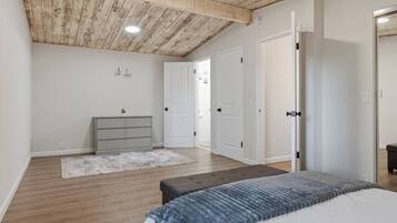 A bedroom with a wooden ceiling, a bed with a blue blanket, a grey dresser, and white doors.