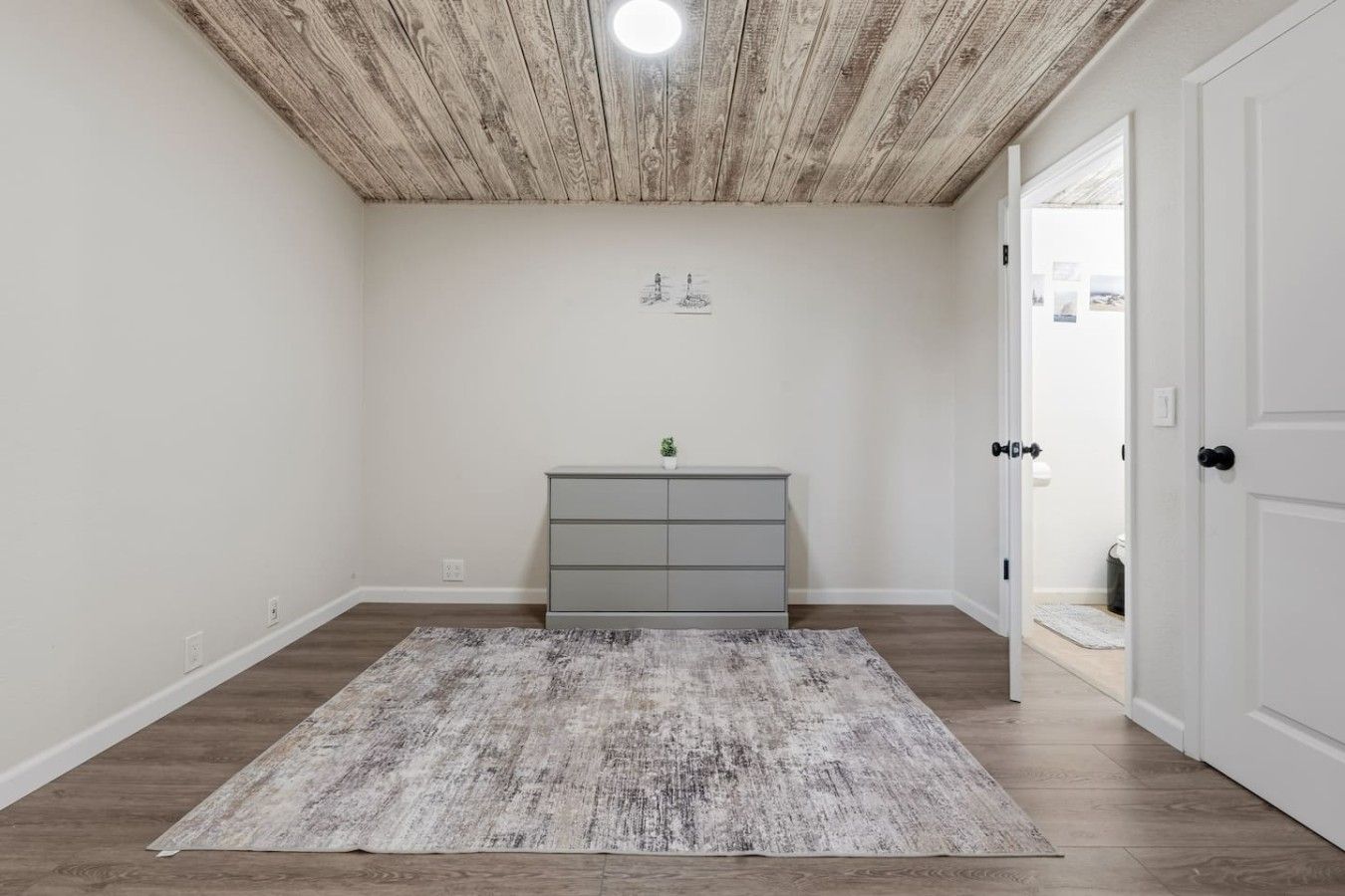 A room with a wooden ceiling, a grey dresser, and a grey rug on a wooden floor.