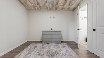 A room with a wooden ceiling, a grey dresser, and a grey rug on a wooden floor.