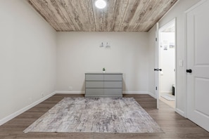 Een kamer met een houten plafond, een grijze dressoir en een grijs vloerkleed op een houten vloer.