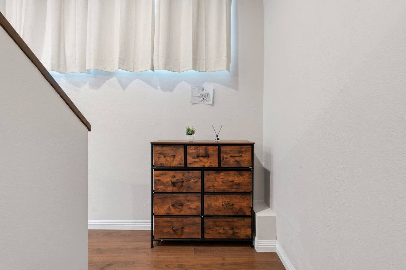 A staircase leading to a room with a wooden chest of drawers, a small plant, and a wall-mounted light switch.