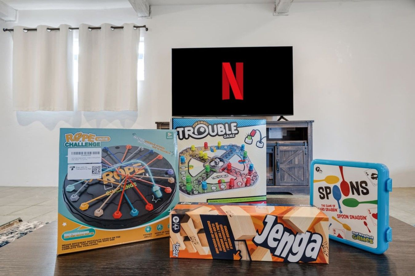 Una habitación con televisor, una mesa con juegos de mesa y una ventana con cortinas.