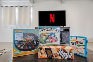 Una habitación con televisor, una mesa con juegos de mesa y una ventana con cortinas.