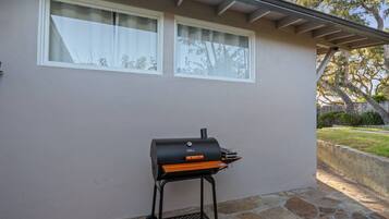 Una parrilla de barbacoa al aire libre frente a una casa con un patio empedrado y una zona cubierta.