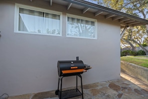 Una parrilla de barbacoa al aire libre frente a una casa con un patio empedrado y una zona cubierta.