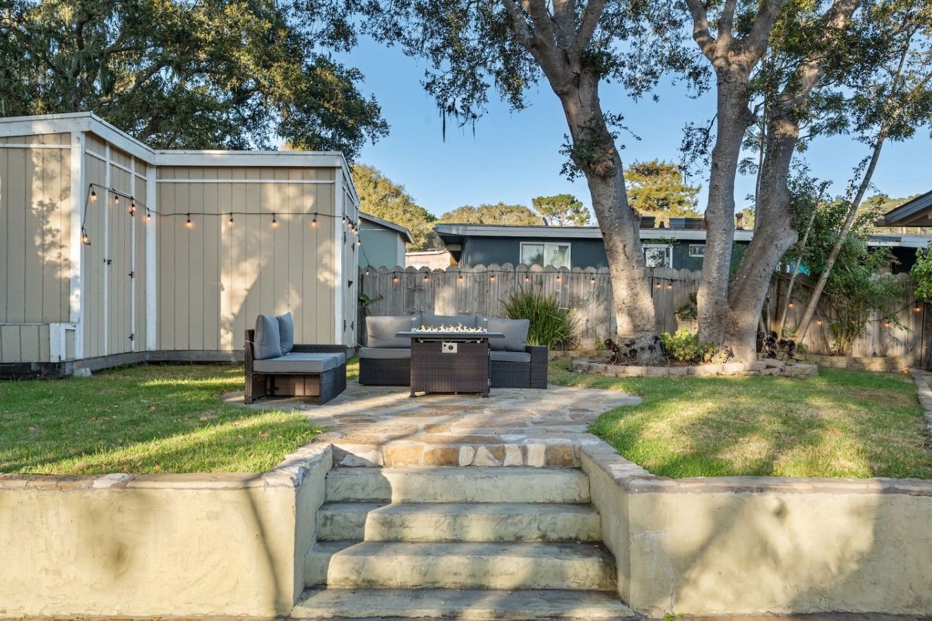A backyard with a stone staircase leading to a patio area, a covered seating area with cushions, and a fire pit.