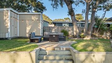 A backyard with a stone staircase leading to a patio area, a covered seating area with cushions, and a fire pit.