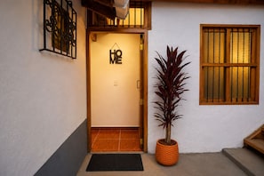 Entrada de hotel com porta de madeira, planta em vaso e janela com barras verticais.