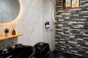 A bathroom with a marble vanity, a black bathtub, a shower area with a stone wall, and a small window. - Reserva Monteverde Rio Negro (Rionegro)