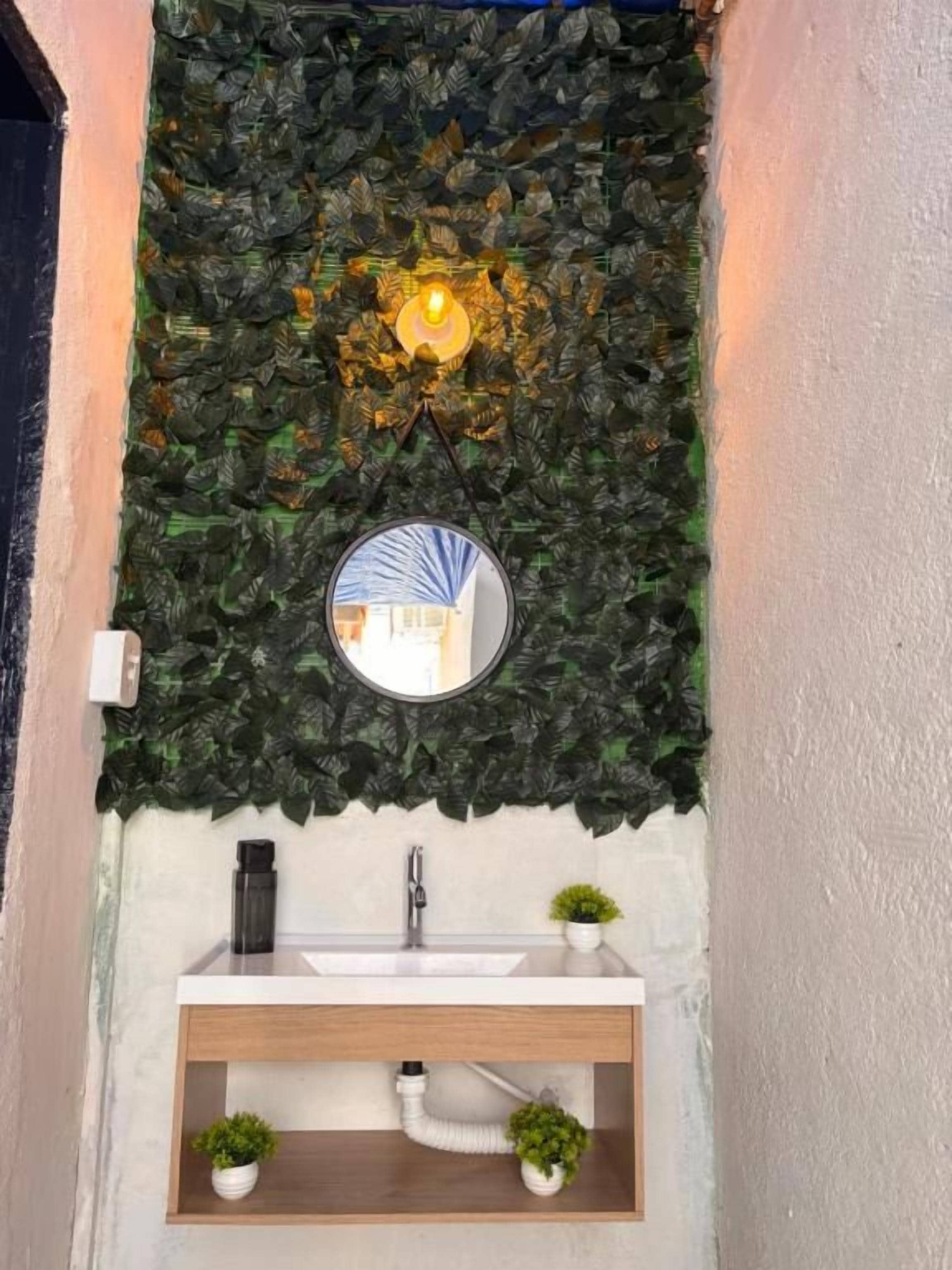Un baño con pared de piedra, un espejo redondo, un lavamanos y dos pequeñas macetas.