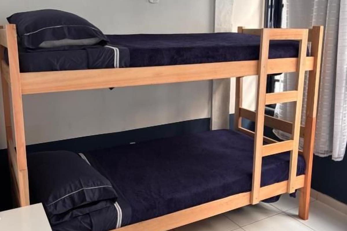 Habitación con literas de madera, una mesita pequeña y una ventana con cortinas.