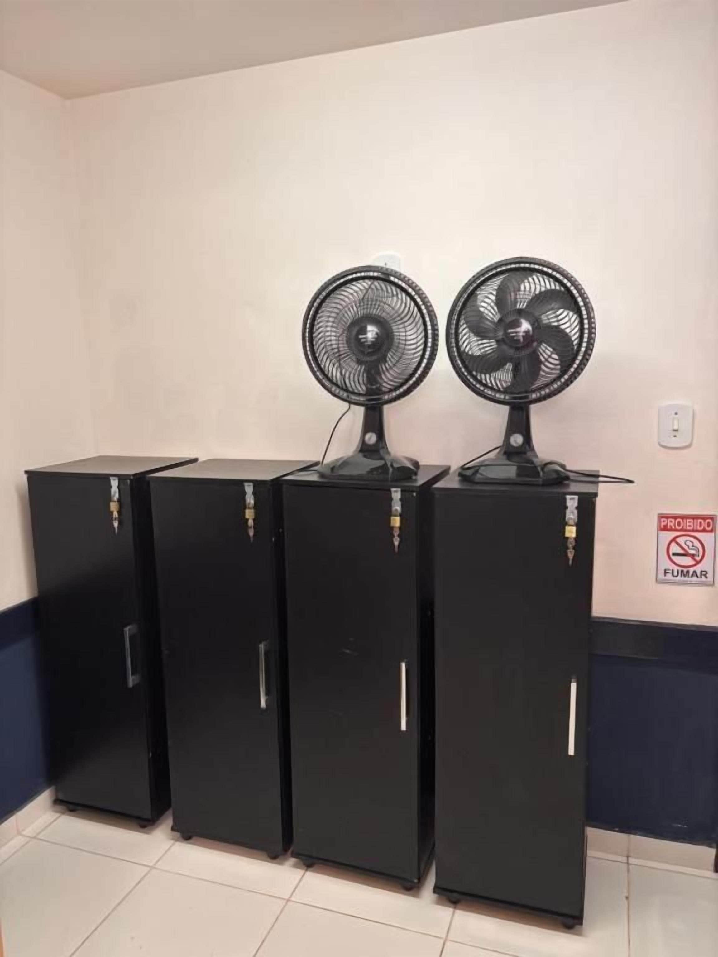 Three black refrigerators with fans on top, a 'Prohibido Fumar' sign, and a tiled floor.