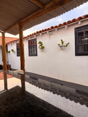 A building with a tiled roof, white walls, and black-framed windows. There are potted plants on the wall and a covered area with a tiled floor. - Primos 2 Suites & Hostel (Búzios)