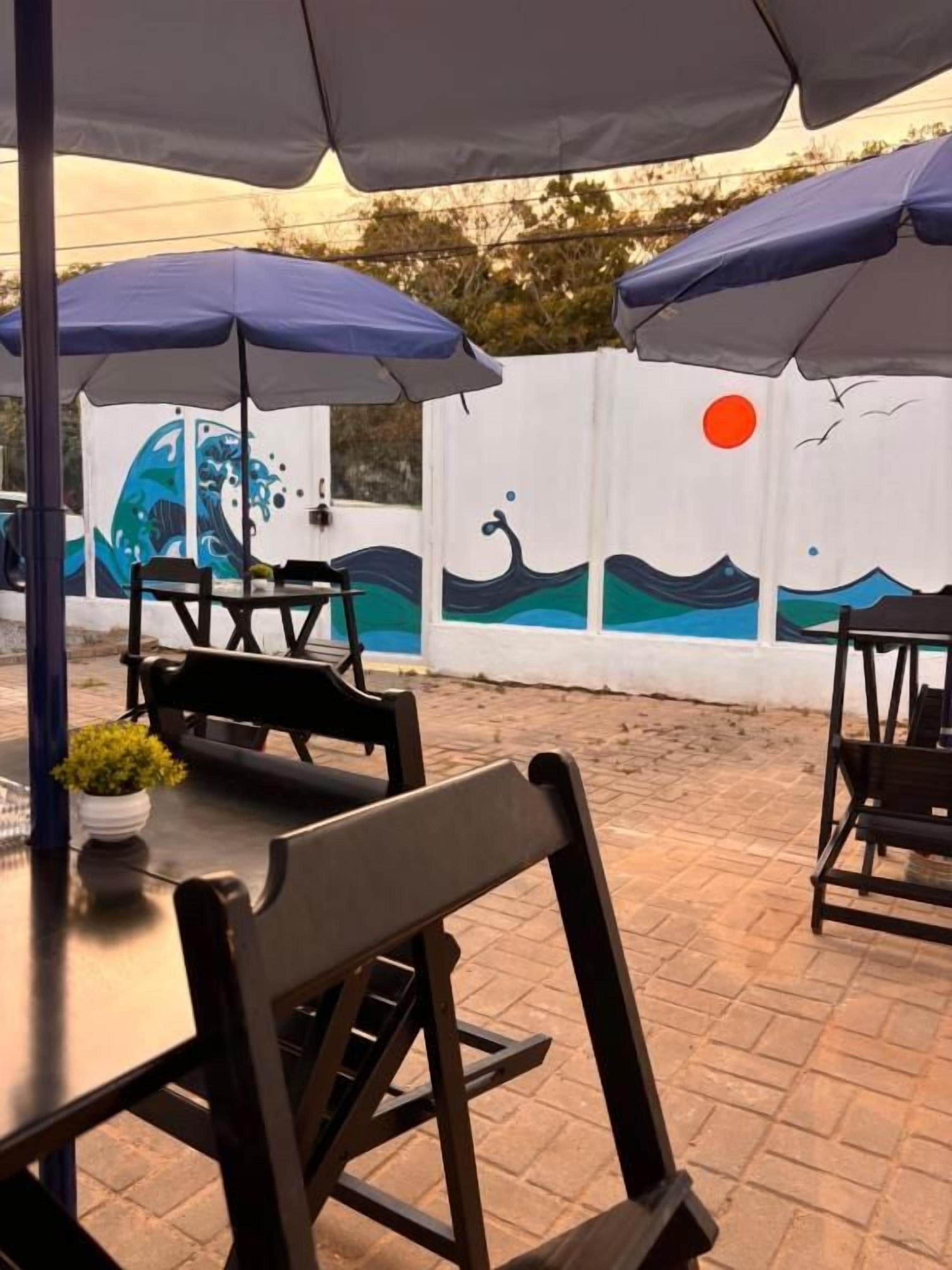An outdoor seating area with tables and chairs under umbrellas, a tiled floor, and a wall with a mural.