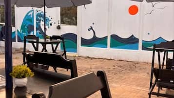 An outdoor seating area with tables and chairs under umbrellas, a tiled floor, and a wall with a mural.