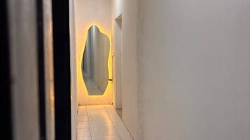 A hallway with white walls and a tiled floor leading to a room with a curved mirror.