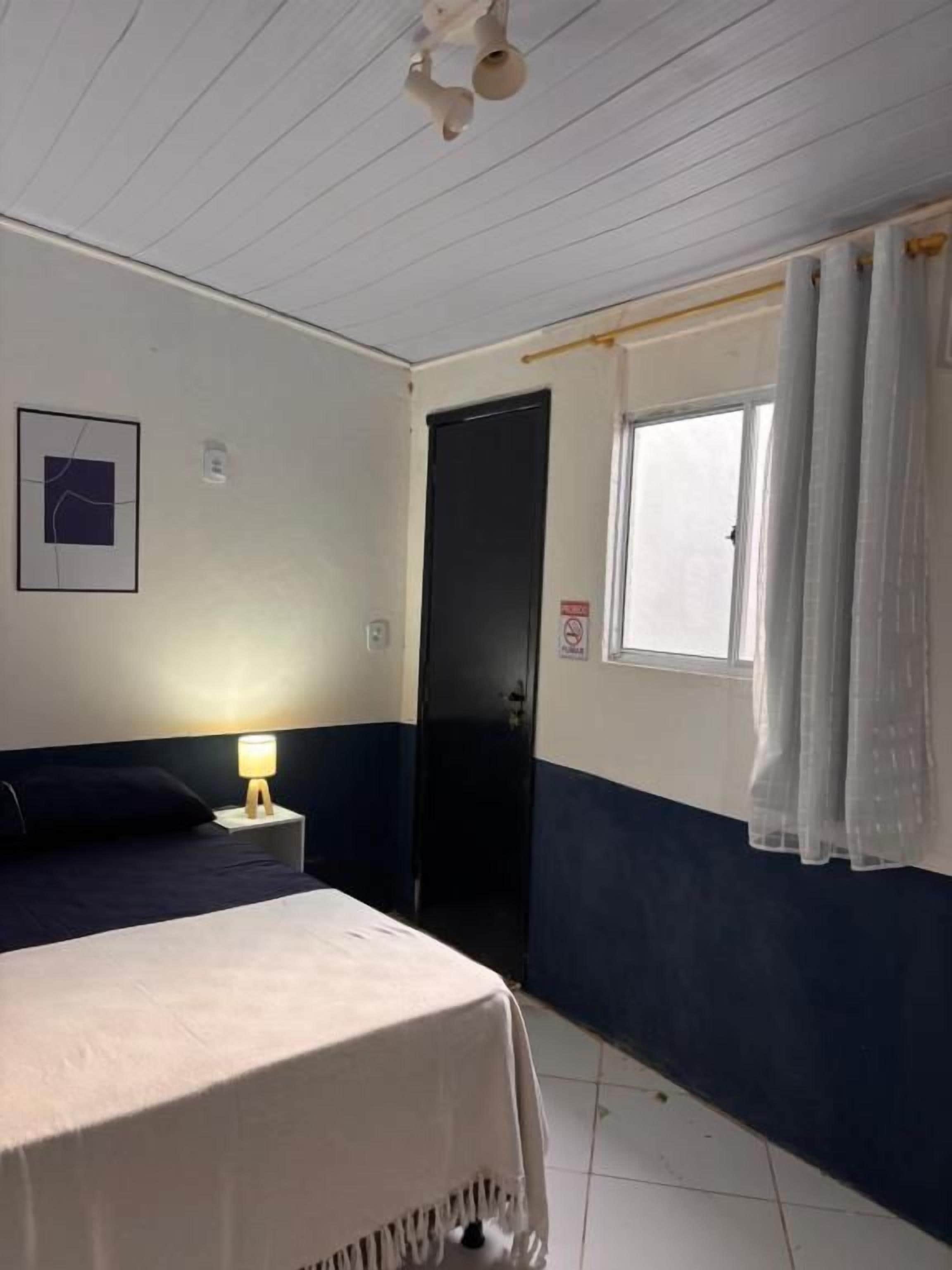 Una habitación de hotel con una cama, una mesita de noche, una ventana con cortinas y una puerta.
