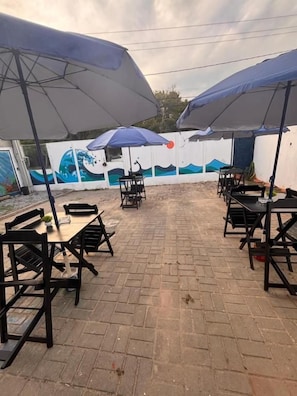 Un patio al aire libre con piso de ladrillo, mesas, sillas y sombrillas.