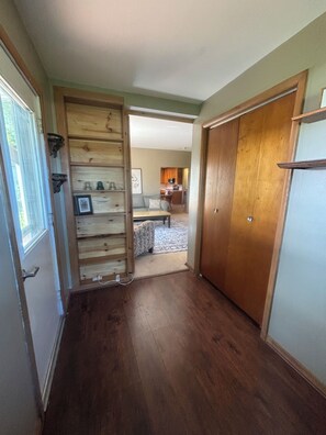 A hallway with wooden flooring leading to a room with a bed and a kitchen area visible in the background.