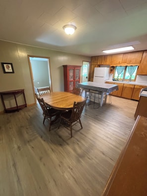 A dining area with a wooden table and chairs, a kitchen with wooden cabinets, and a window with curtains.