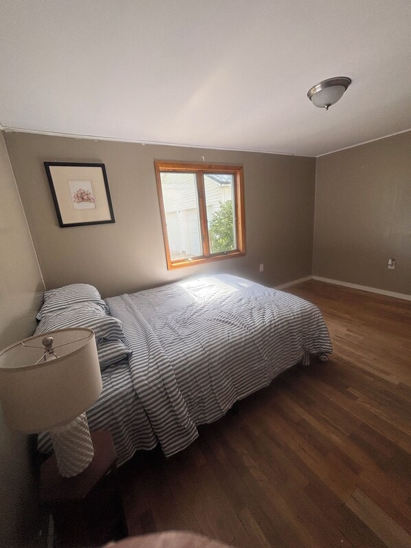A bedroom with a single bed, a nightstand, a lamp, a window, and a ceiling light fixture.