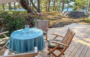A wooden deck with a round table and chairs, a hanging chair, and a view of a lake and trees. - 3 bedroom nice home in Strömstad (Strömstad)