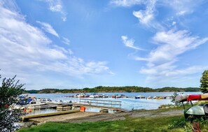 Une jetée au bord du lac, avec des bateaux amarrés, un quai et une zone herbeuse où est installée une tente.