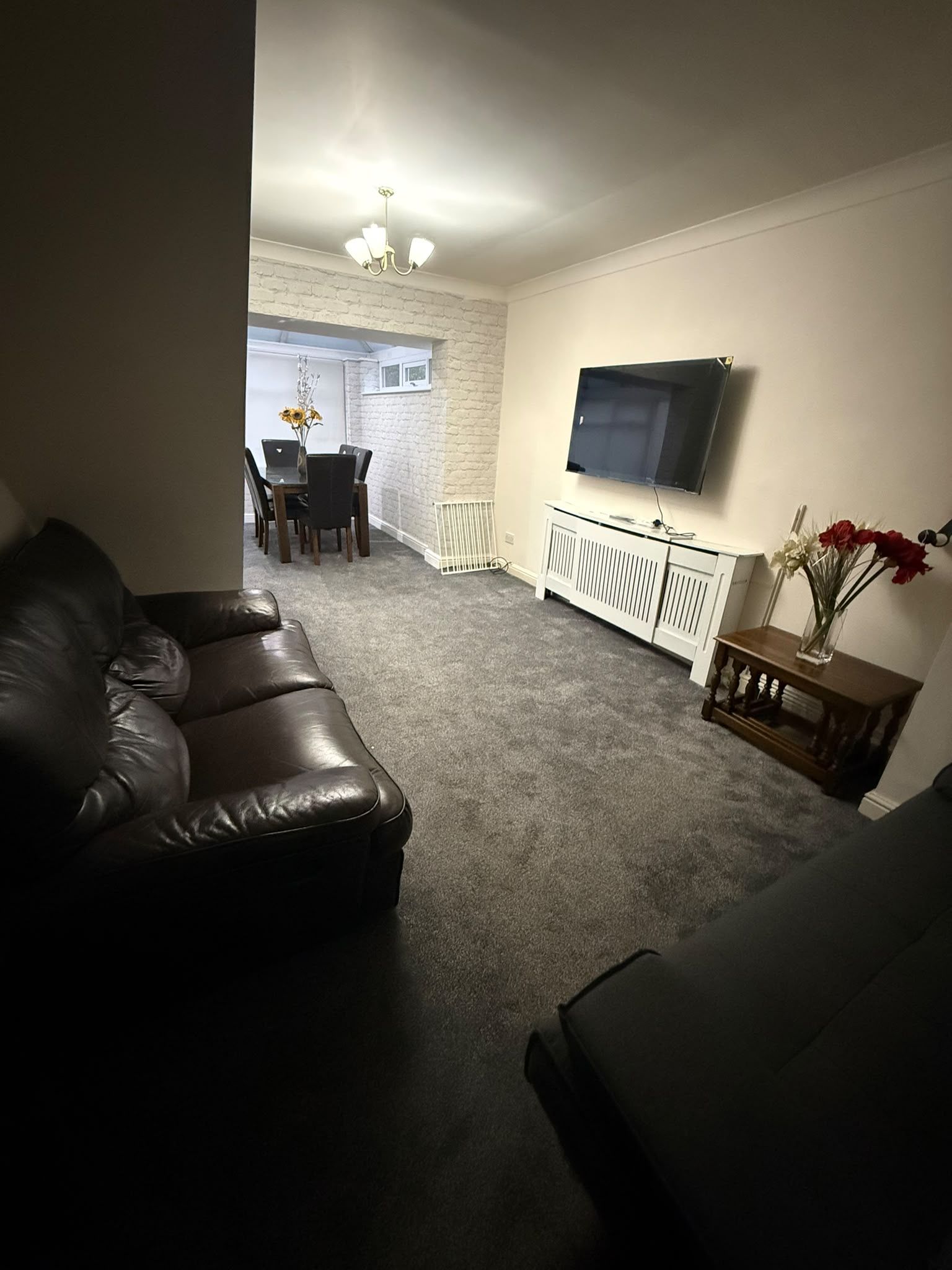 Uma sala de estar com sofá de couro, área de jantar com mesa e cadeiras, radiador branco e televisão de tela plana na parede.